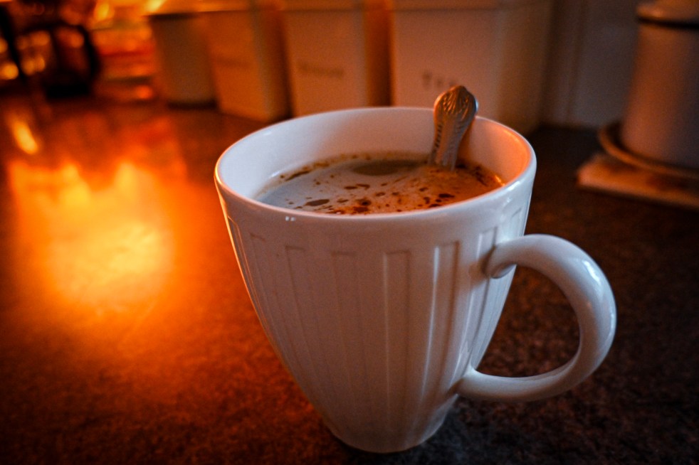 Coffee in a mug with a spoon, on a counter top with a light shining on the surface